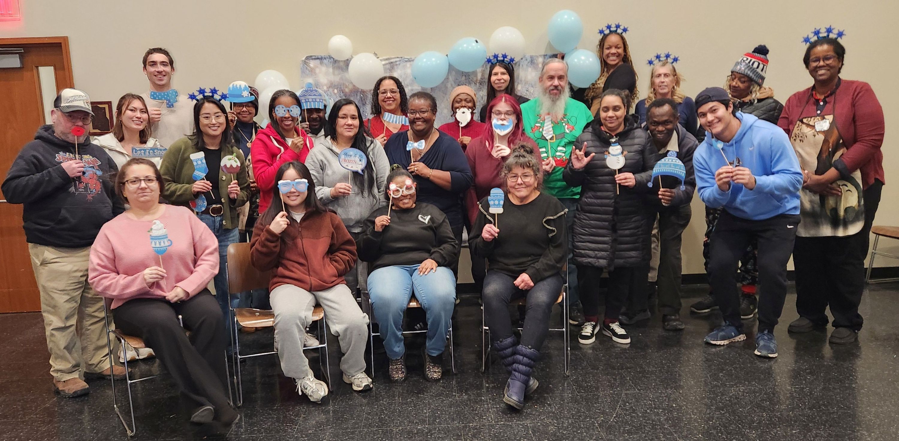 Image of happy people in festive attire standing in front of wall with balloons above their head.