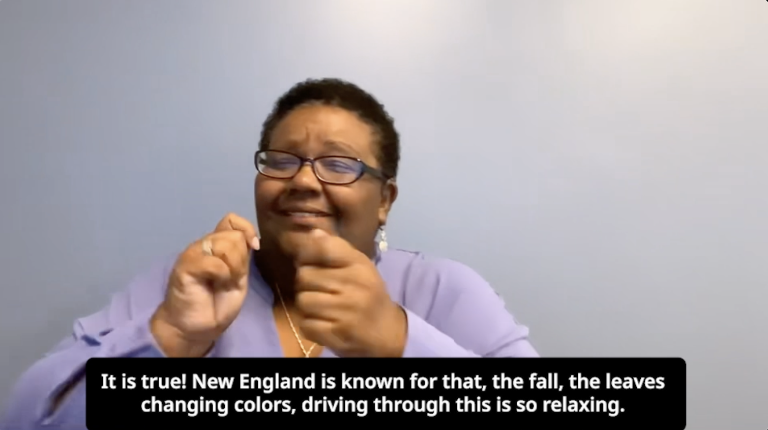 DEAF, Inc. Executive Director, Darian, sits in front of a light blue wall. She wears a purple sweater and black glasses. The captioned text below her says, “It is true! New England is known for that, the fall, the leaves changing colors, driving through this is so relaxing.” DEAF, Inc. Executive Director, Darian, sits in front of a light blue wall. She wears a purple sweater and black glasses. The captioned text below her says, “It is true! New England is known for that, the fall, the leaves changing colors, driving through this is so relaxing.”