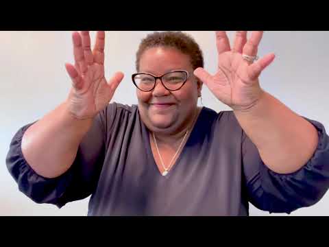 June 2024 DEAF, Inc. Website Announcement - DEAF, Inc. Executive Director Darian Gambrell stands in front of a grey background and waves her hands. She is wearing a navy blue shirt, silver necklace, and black glasses.